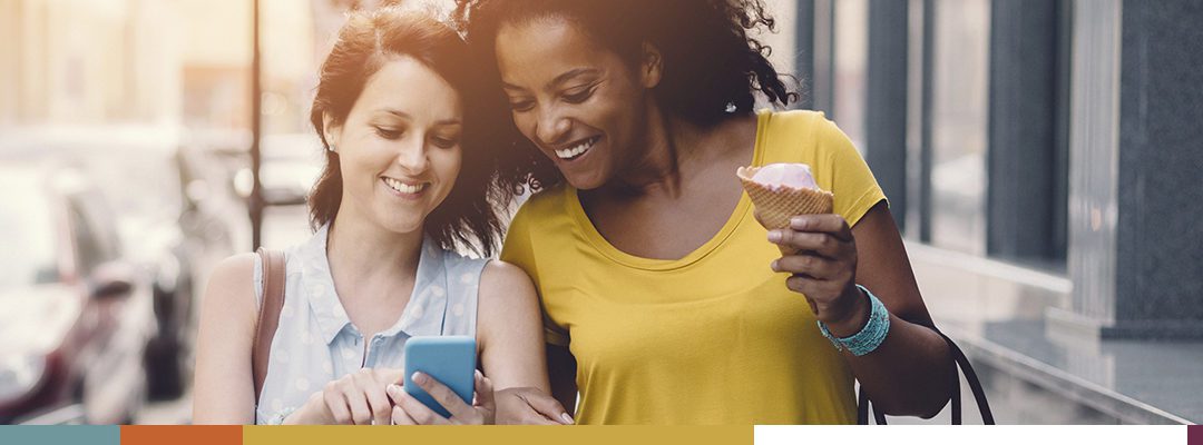 Two friends smiling and sharing a moment while looking at a phone.