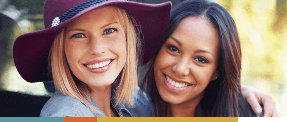 Two women smiling closely, one wearing a purple hat.