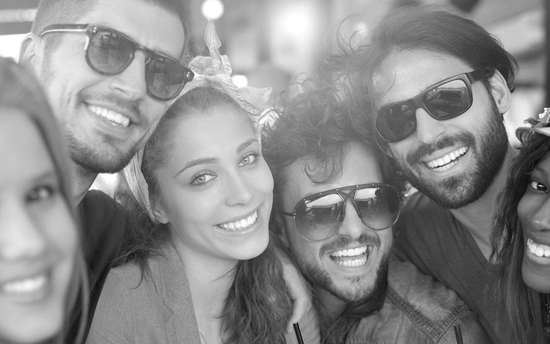 Four friends smiling together, wearing sunglasses in a lively setting.