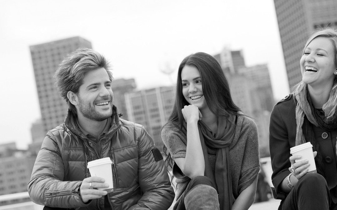 A man and woman smiling and chatting outdoors with coffee cups.