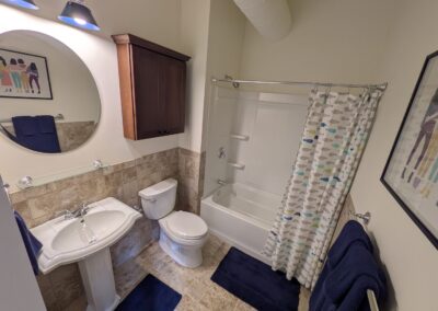 Clean bathroom with pedestal sink, toilet, and bathtub with patterned shower curtain.