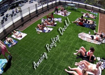 People sunbathe on a rooftop deck with green artificial grass.
